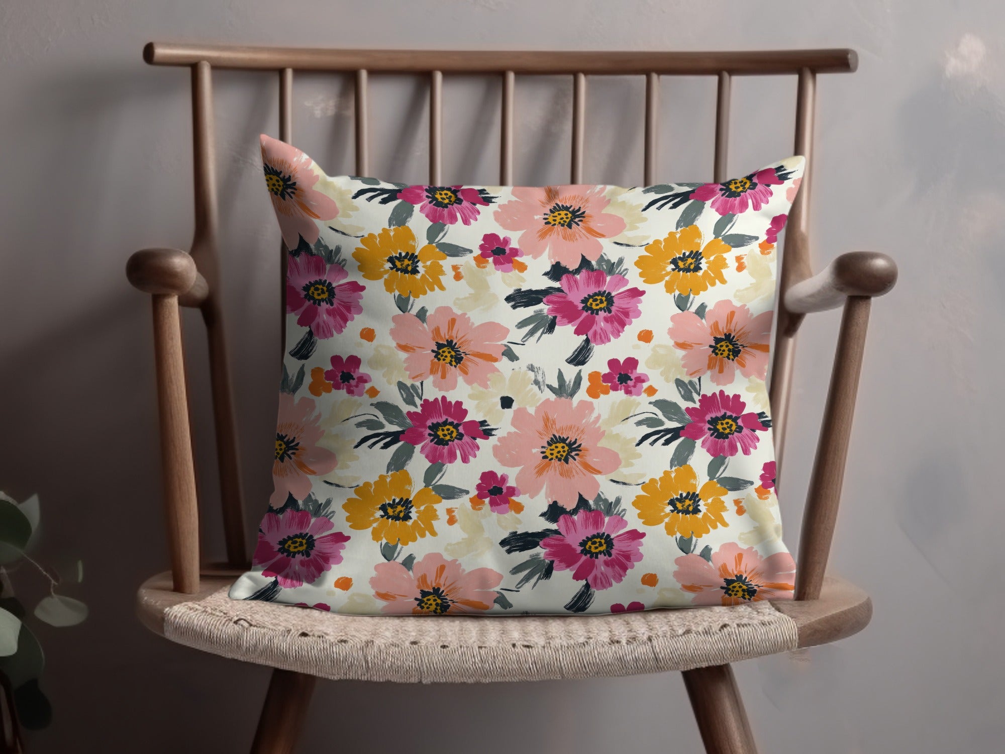 Floral accent pillow with pink, yellow, and orange flowers on a light background.