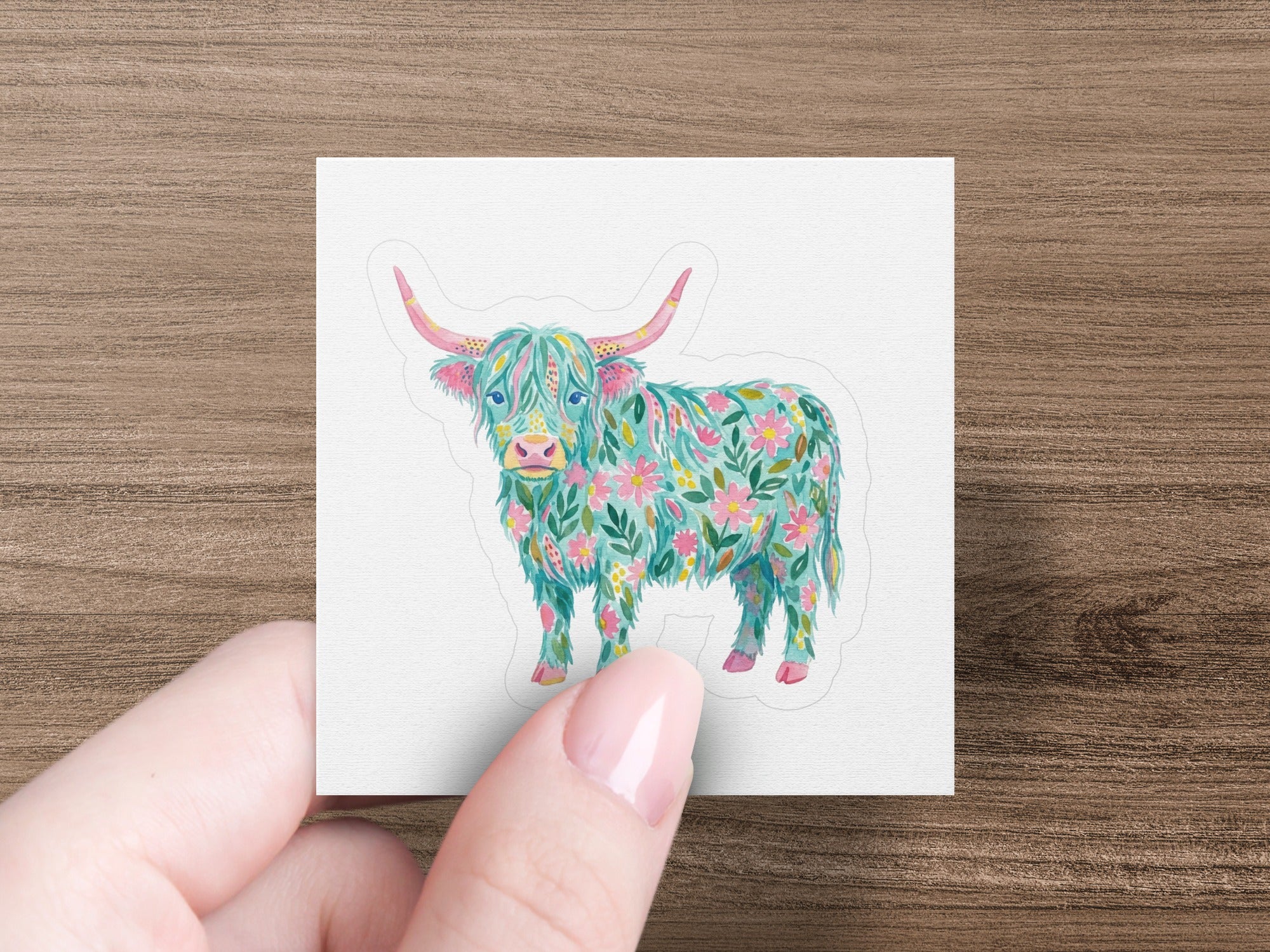 Highland cow sticker with floral pattern, held by a hand.