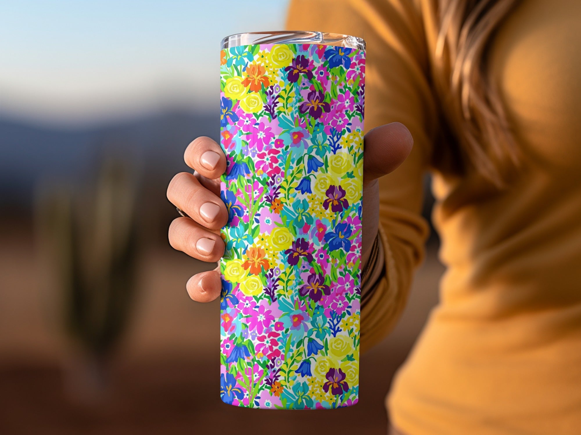 Woman holding a colorful floral tumbler with blue, pink, and yellow flowers.