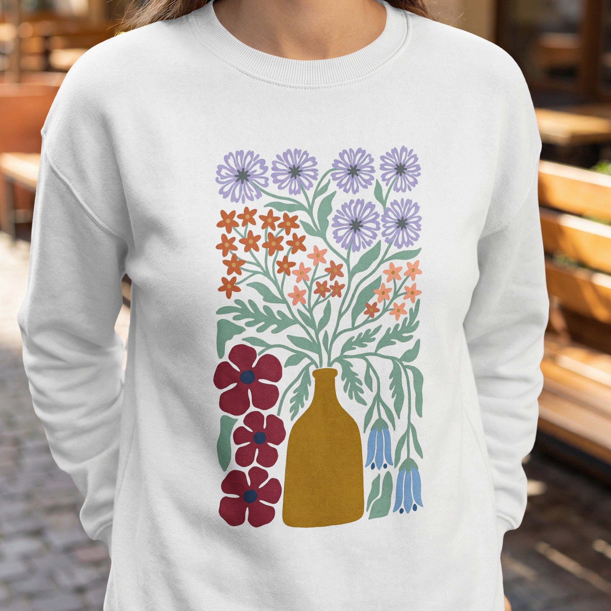 White sweatshirt with a stylized floral bouquet in a mustard yellow vase.