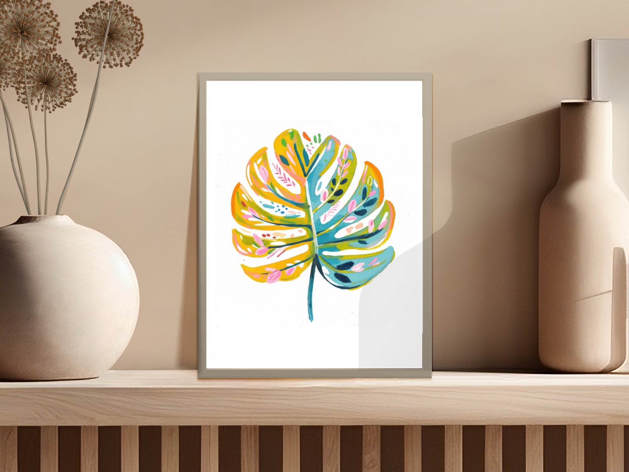 Colorful monstera leaf painting in a minimalist frame on a shelf.