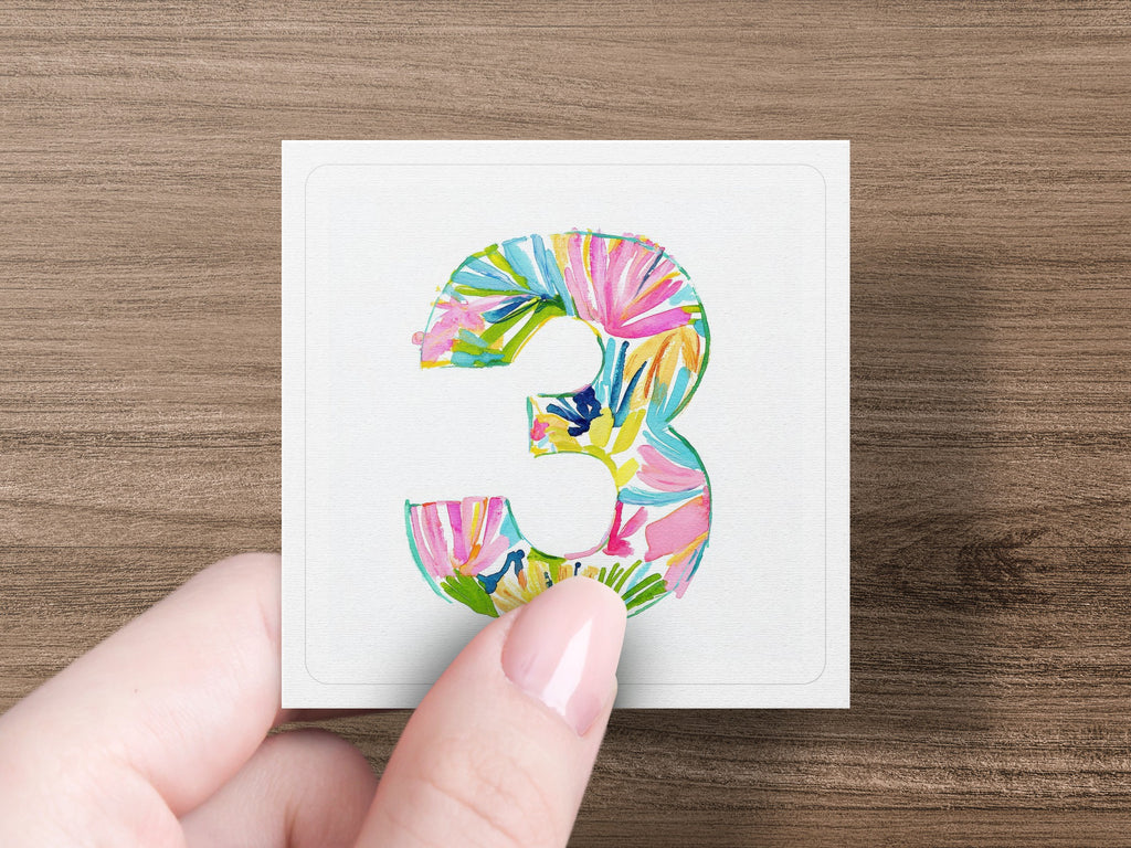 Hand holding square card with colorful floral number 3.
