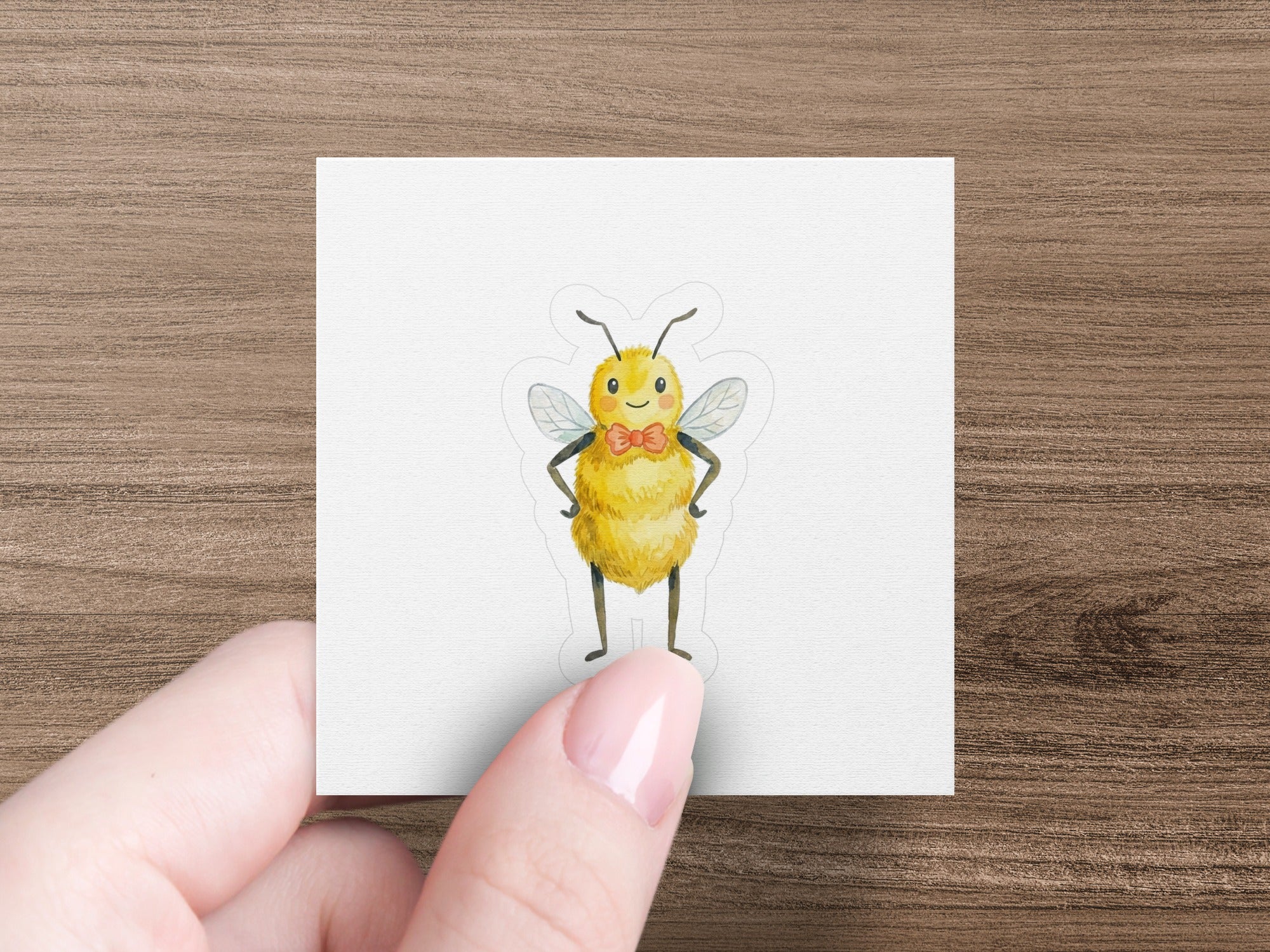 Cute cartoon bee wearing a bowtie, sticker on white paper held by fingers.