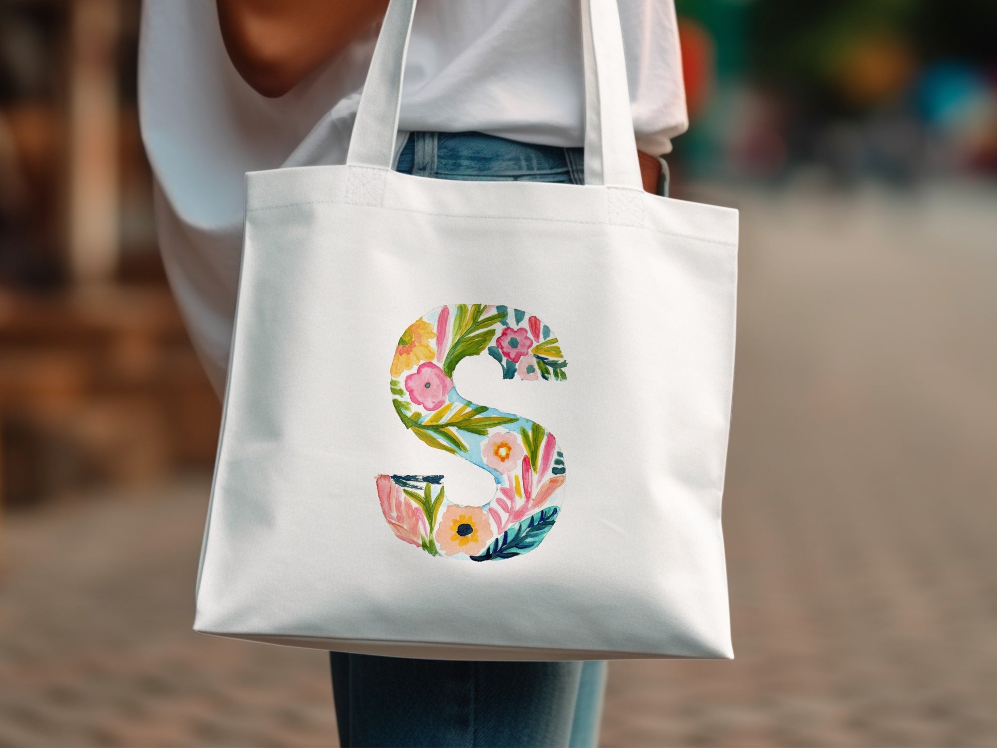 White tote bag with large colorful floral letter "S" design.