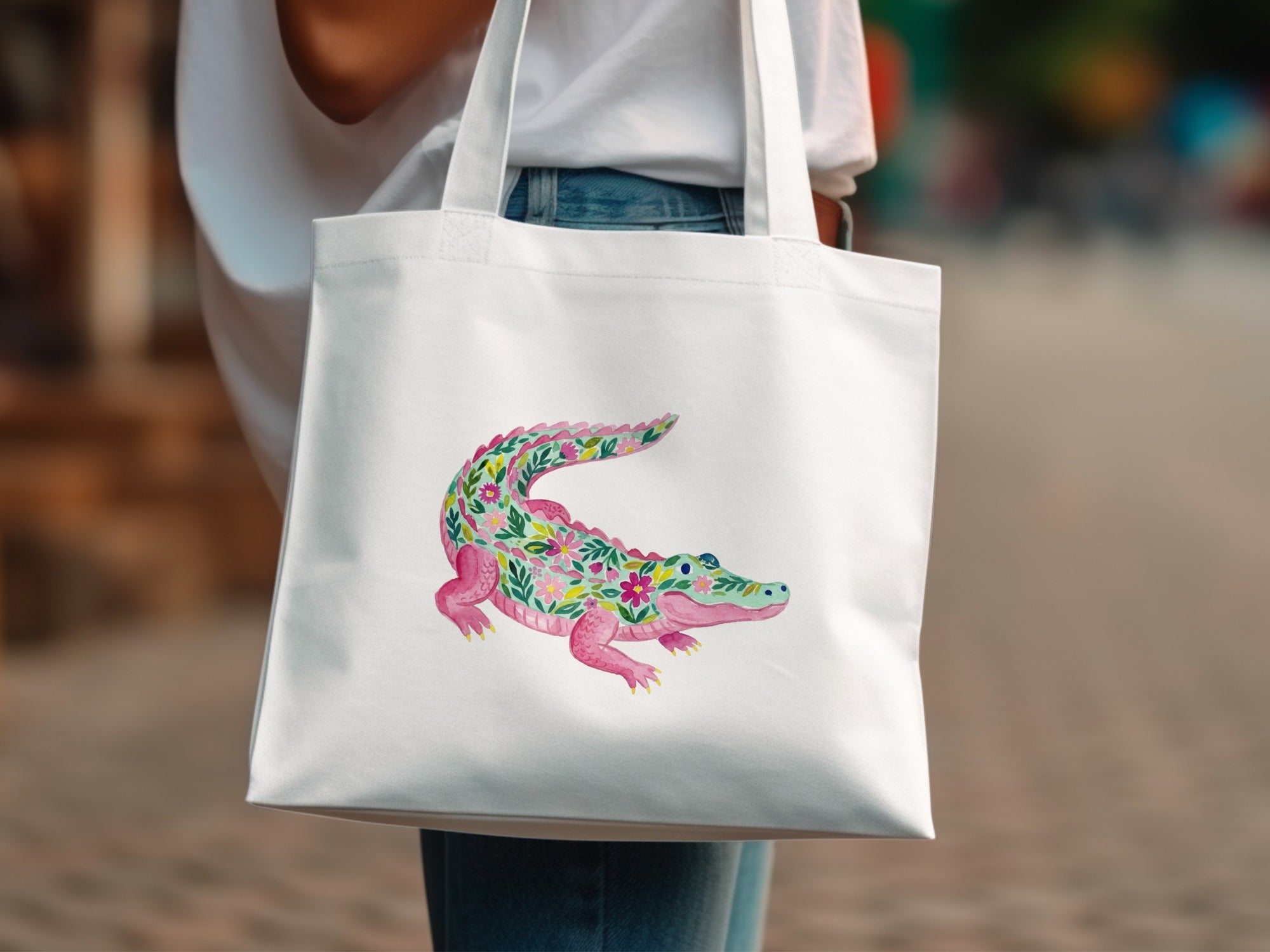 White tote bag with a pink alligator design made of colorful flowers.