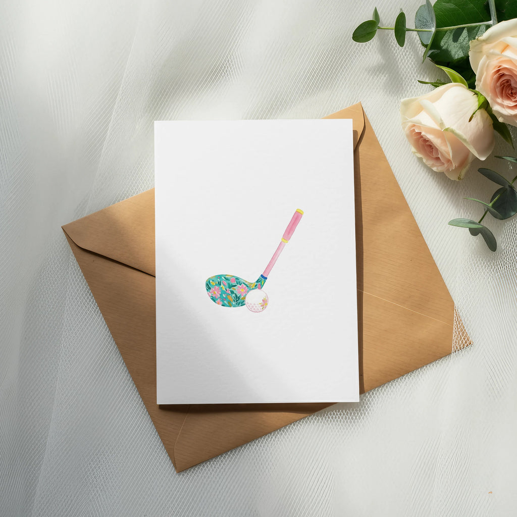 Golf club with floral pattern and golf ball on blank card, next to roses.