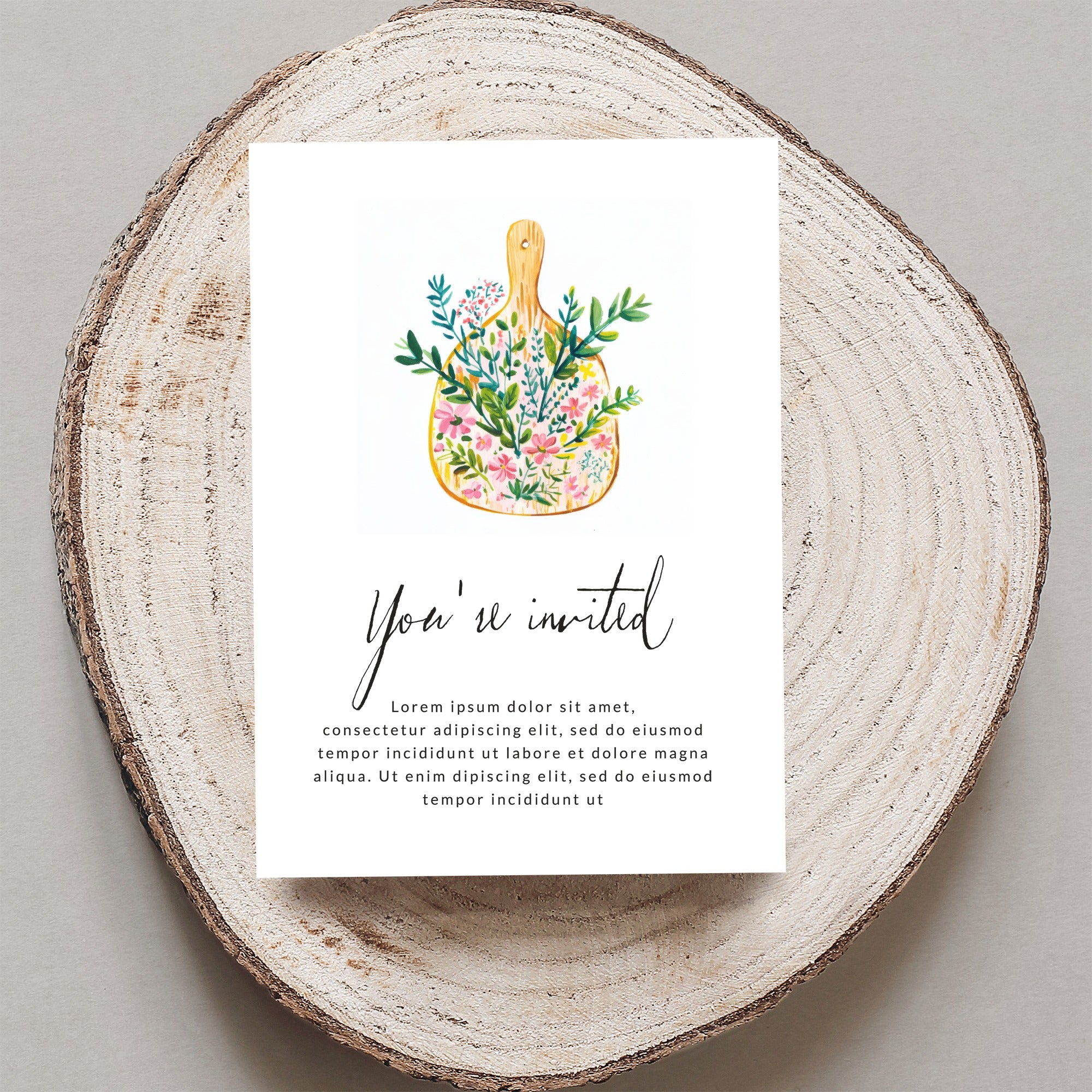 Invitation card with floral illustration and placeholder text, on wood slice.