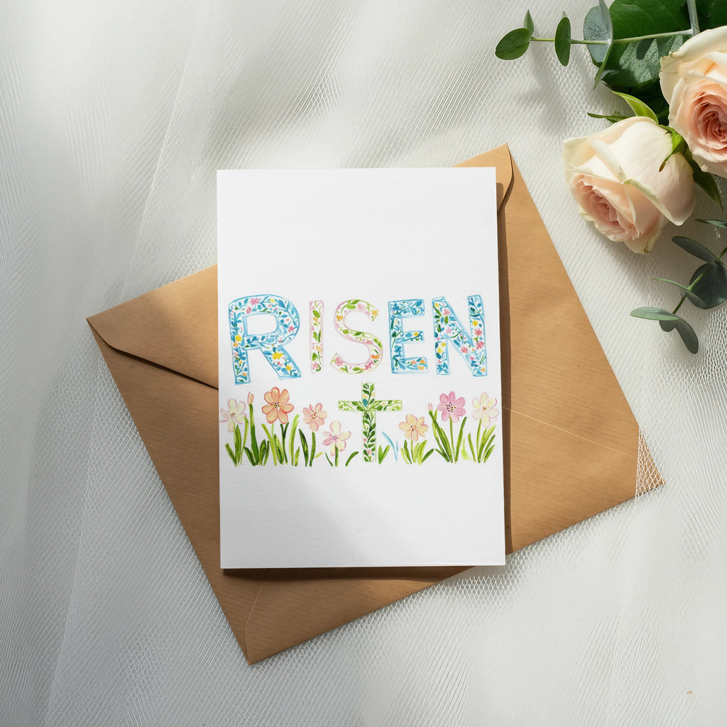 Card with "RISEN" and a floral cross on a kraft envelope.