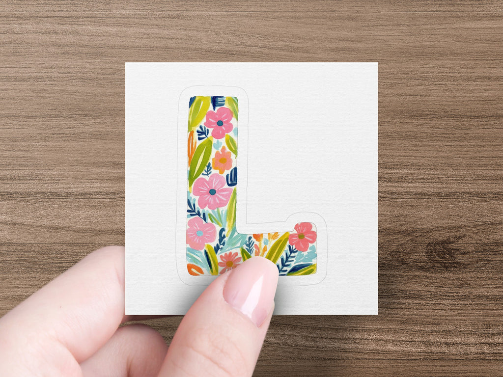 Letter L sticker with colorful floral pattern held by a hand.