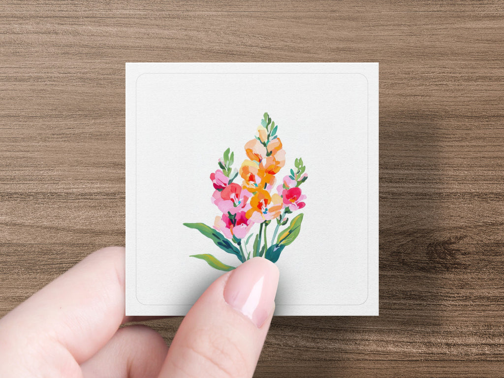 Hand holds small square card with colorful floral illustration.