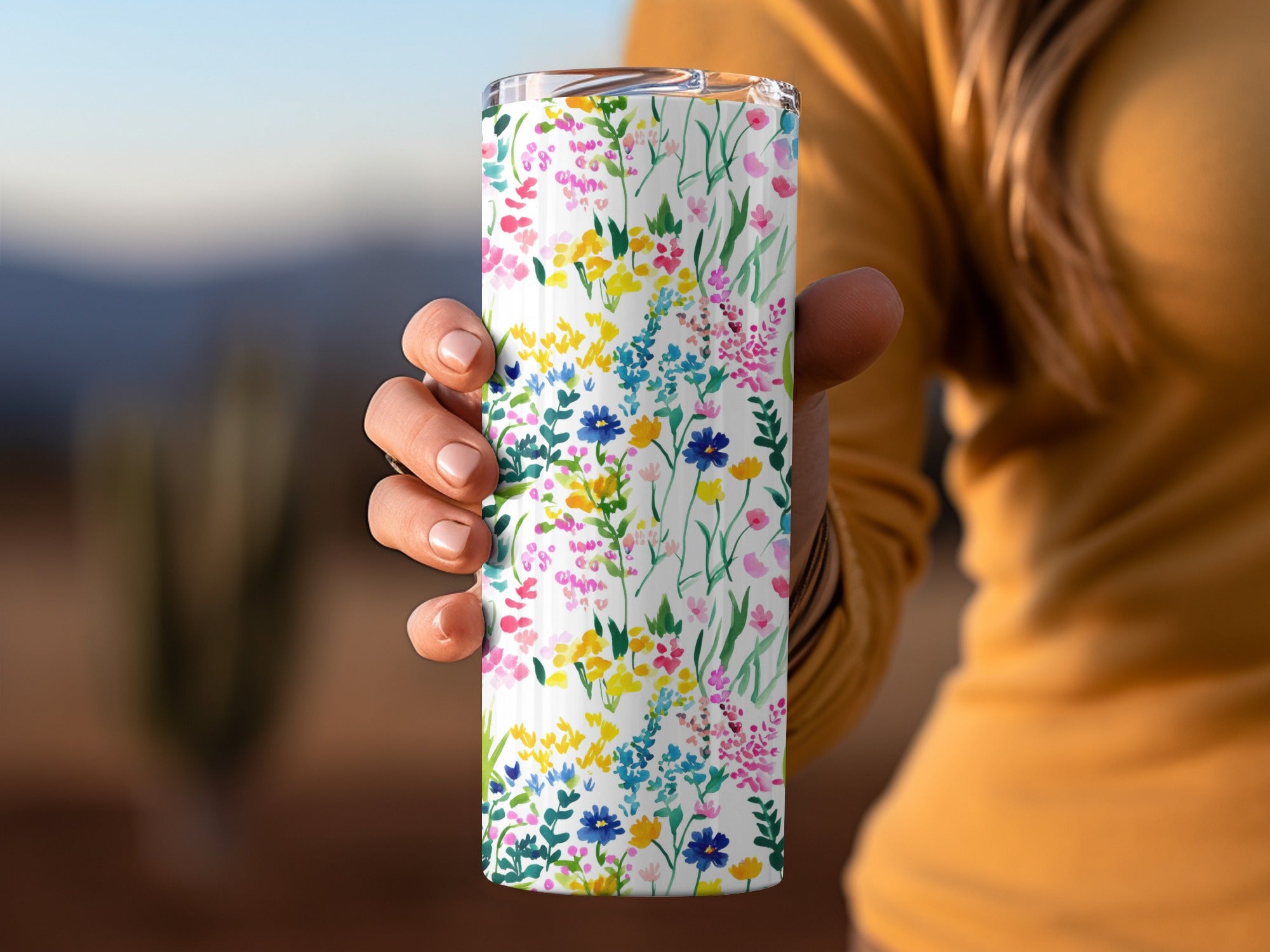 Woman holding a floral-patterned tumbler with pink, yellow, and blue wildflowers.