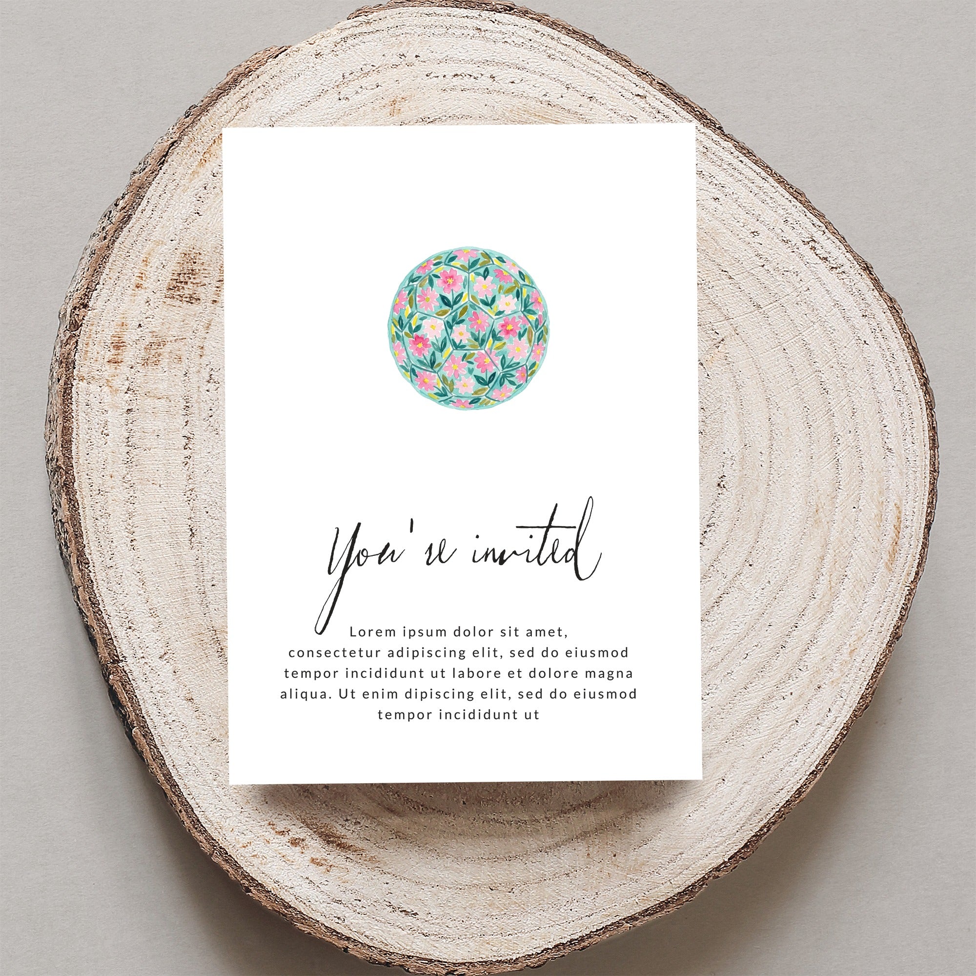 Invitation with "You're invited" text and floral illustration on wood slice.