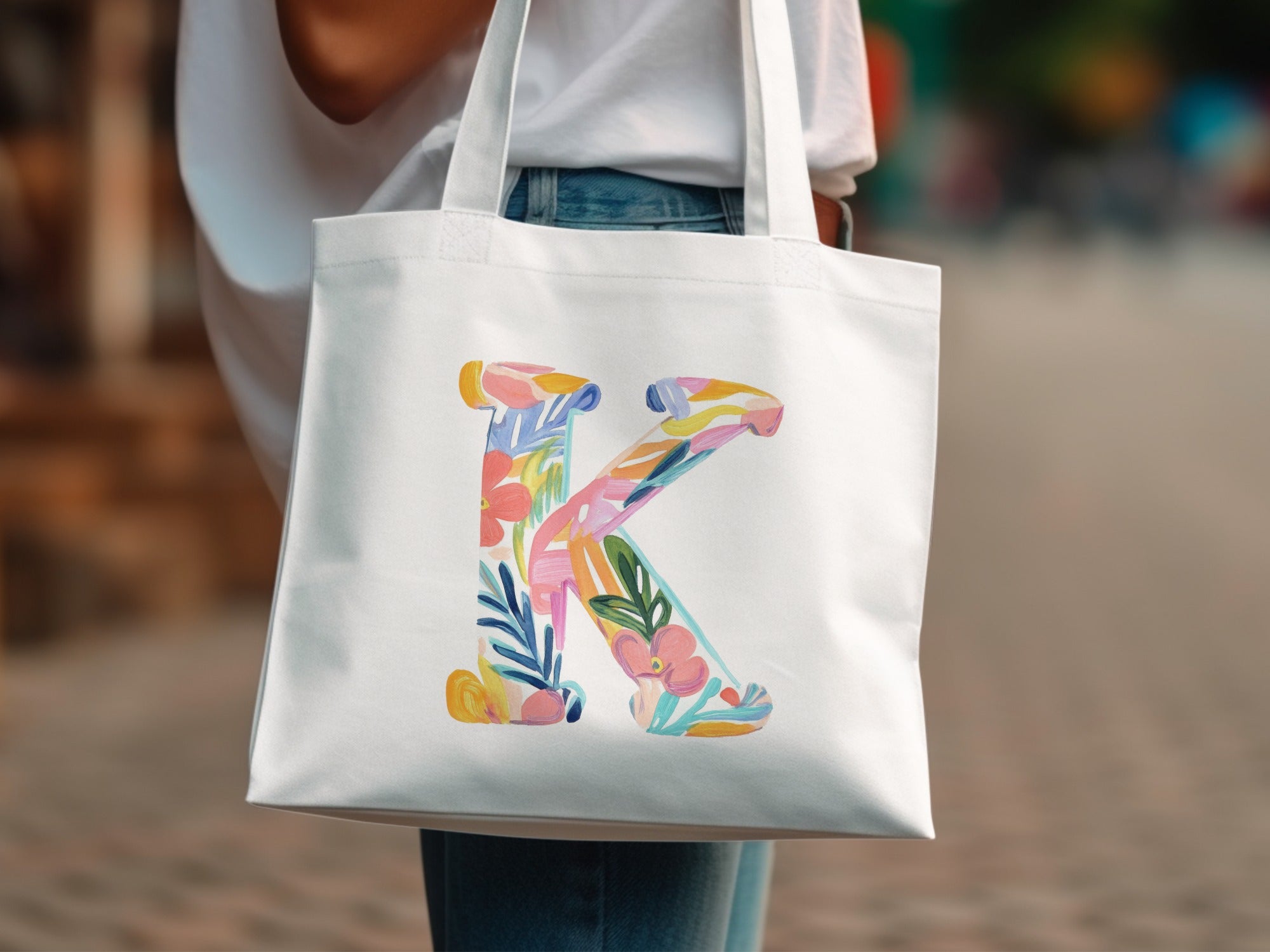 White tote bag with a large, colorful floral letter K design.