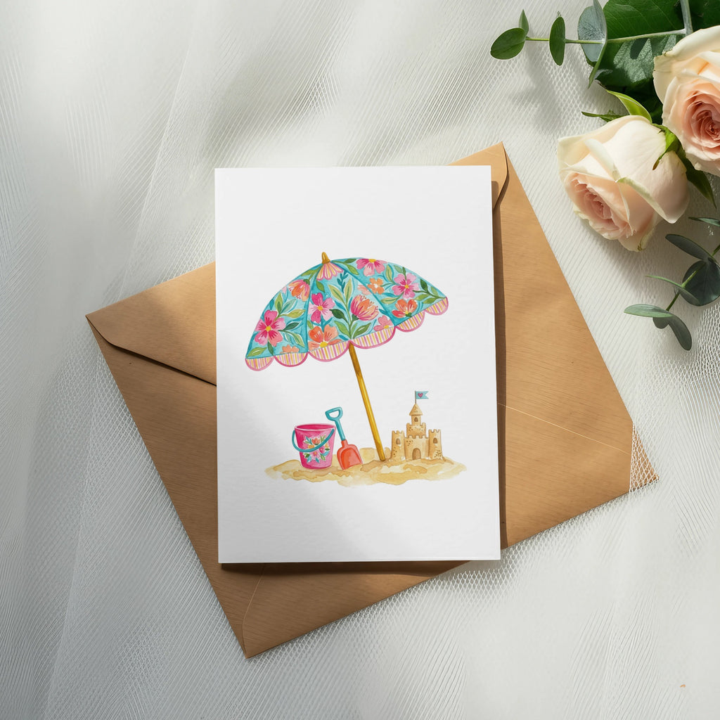 Watercolor illustration of a beach umbrella and sandcastle on a card.