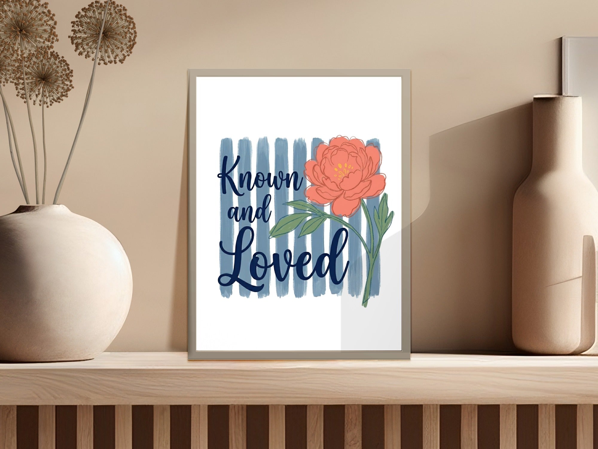 Framed print with coral peony and "Known and Loved" text on blue stripes.