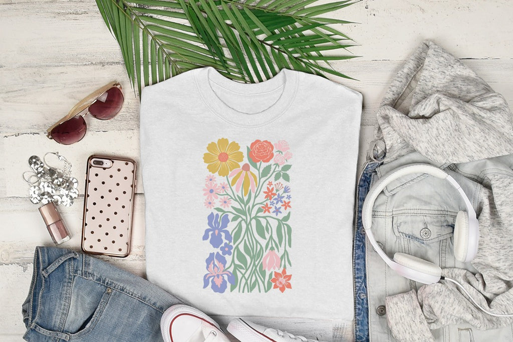 White t-shirt with a colorful floral graphic, laid flat with headphones and jeans.