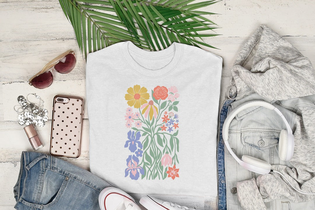White t-shirt with a colorful floral graphic, laid flat with headphones and jeans.