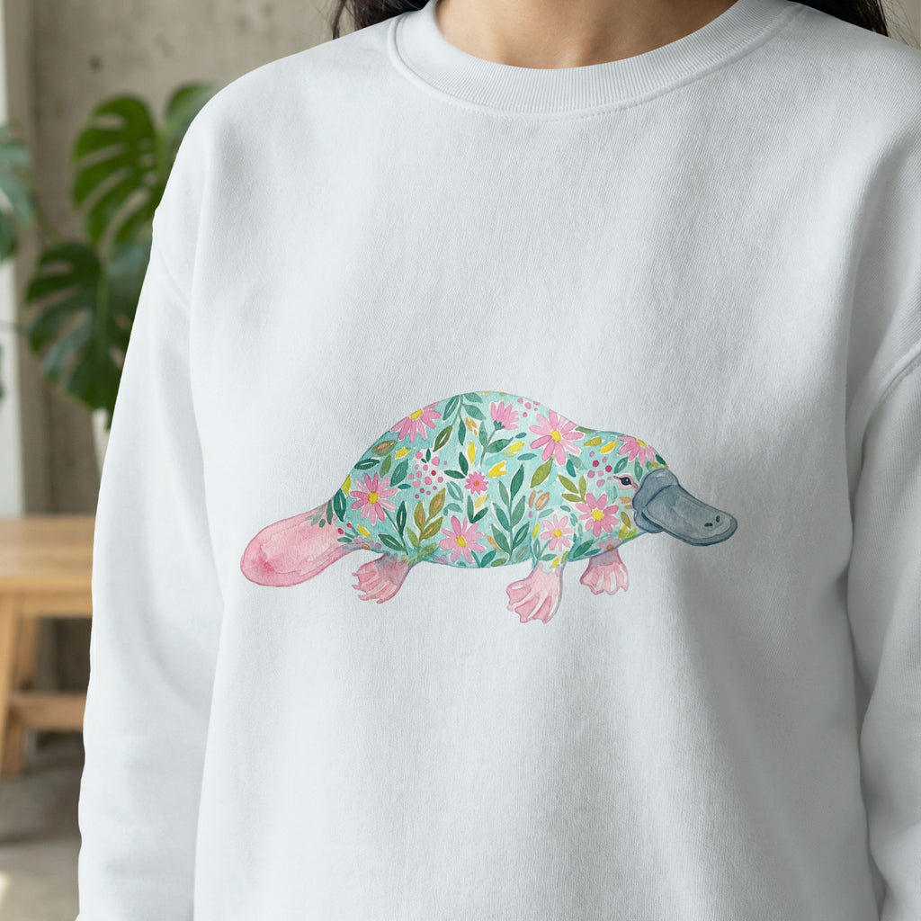 White sweatshirt with a watercolor platypus design featuring floral patterns.
