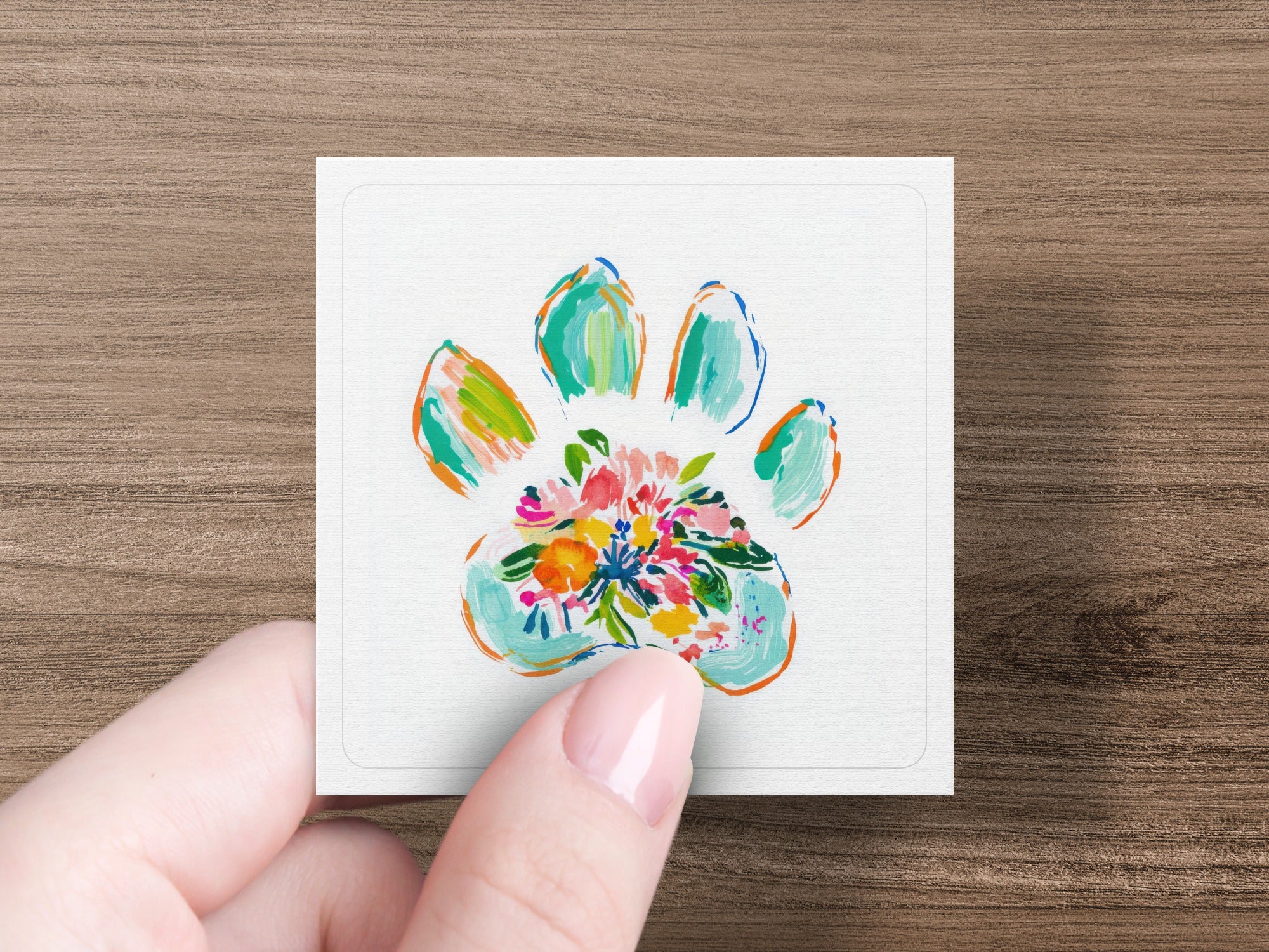 Floral paw print design on a square card held by a hand.