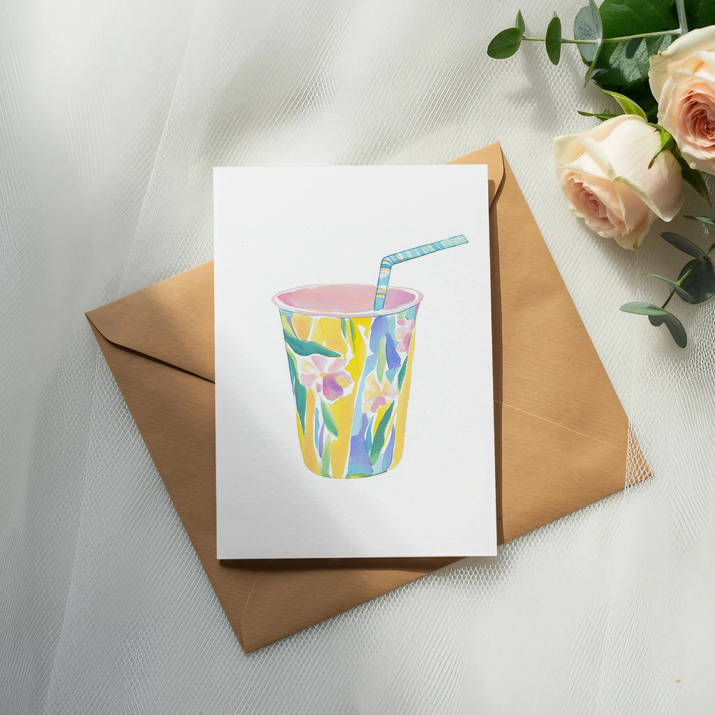 Cup with floral pattern, straw, on brown envelope with roses and eucalyptus.