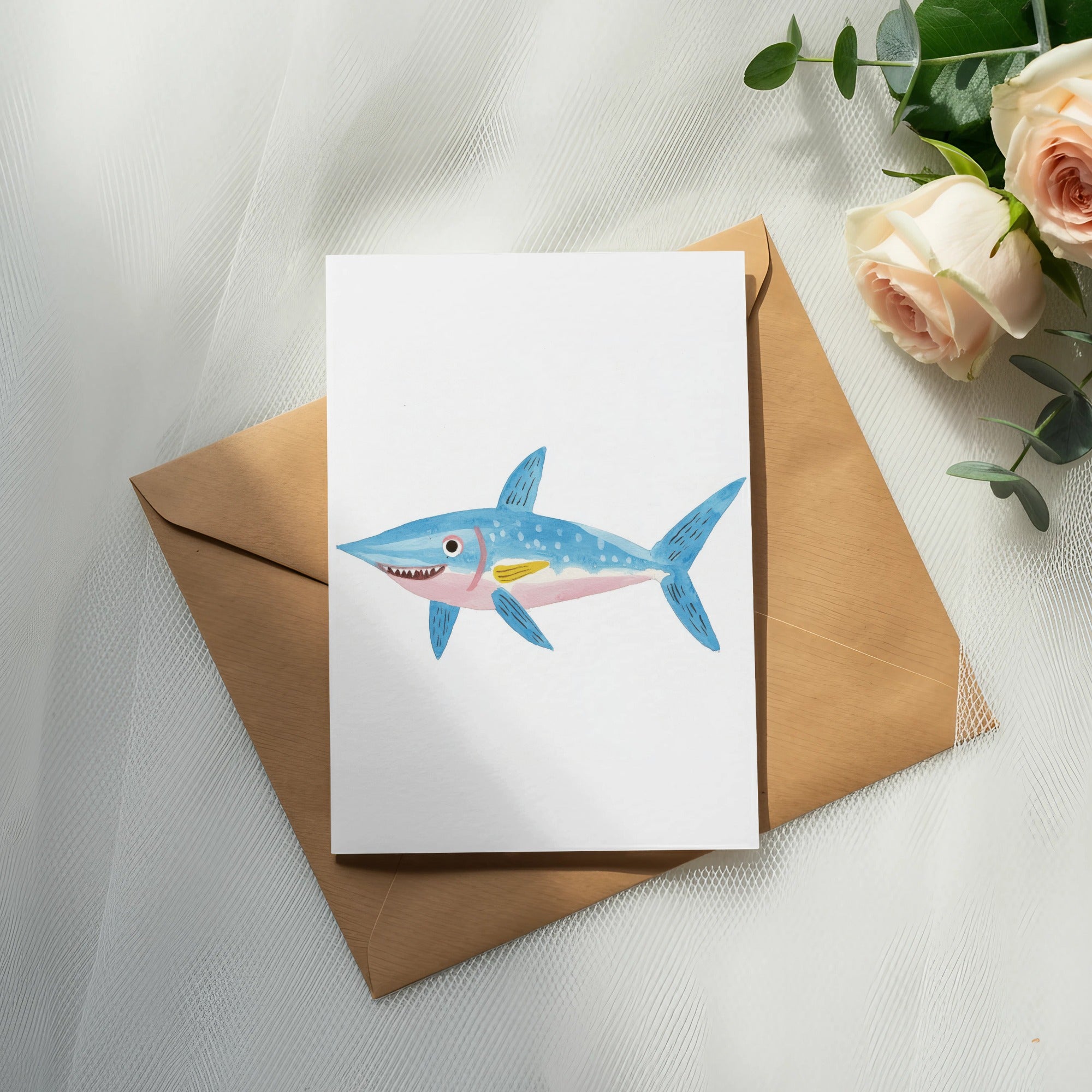 Watercolor illustration of a blue shark on a card, placed on a brown envelope.