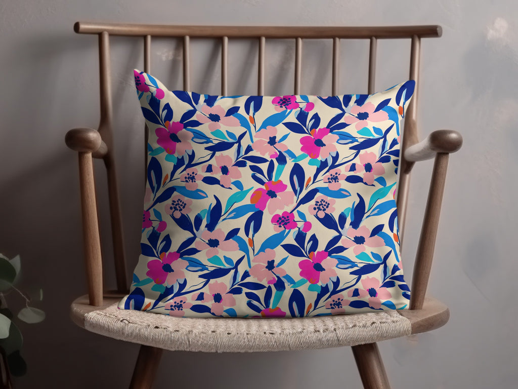 Cream pillow with vibrant pink and blue floral pattern on wooden chair.