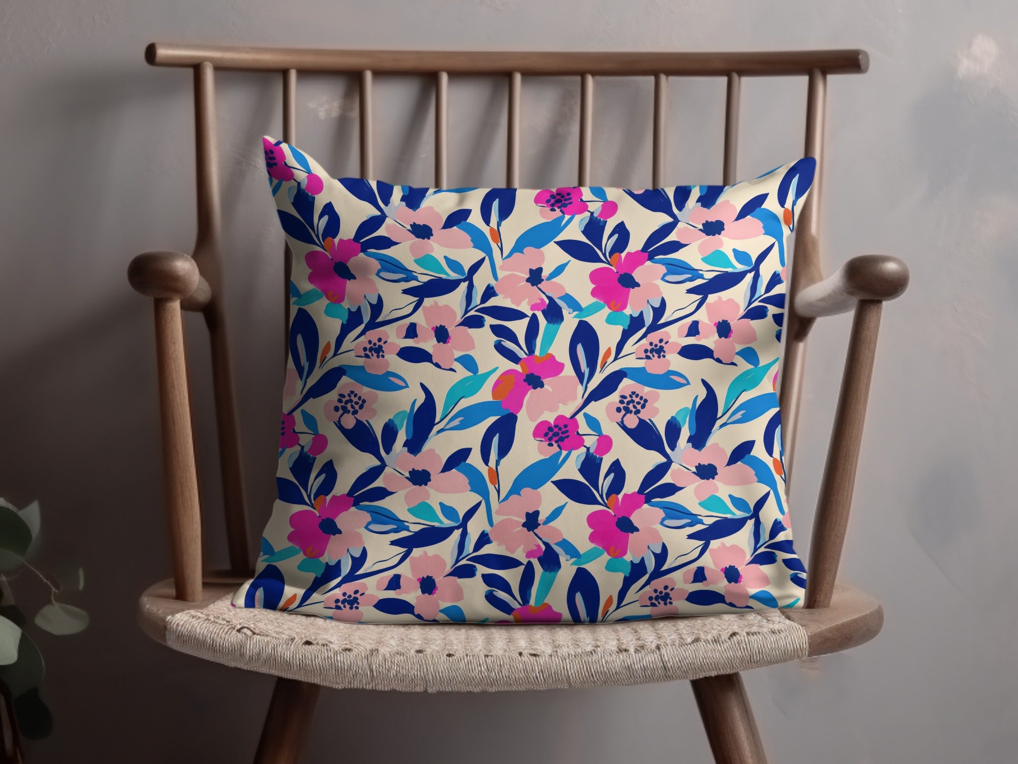 Cream pillow with vibrant pink and blue floral pattern on wooden chair.