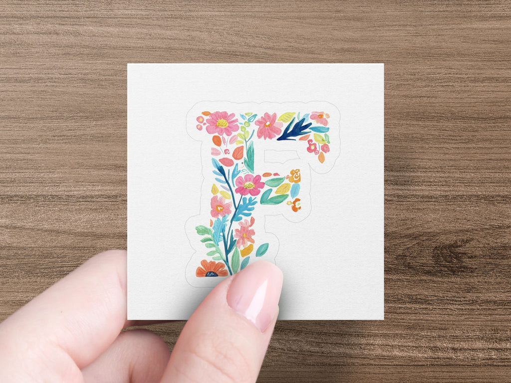 Floral letter F sticker in a hand against a white background.