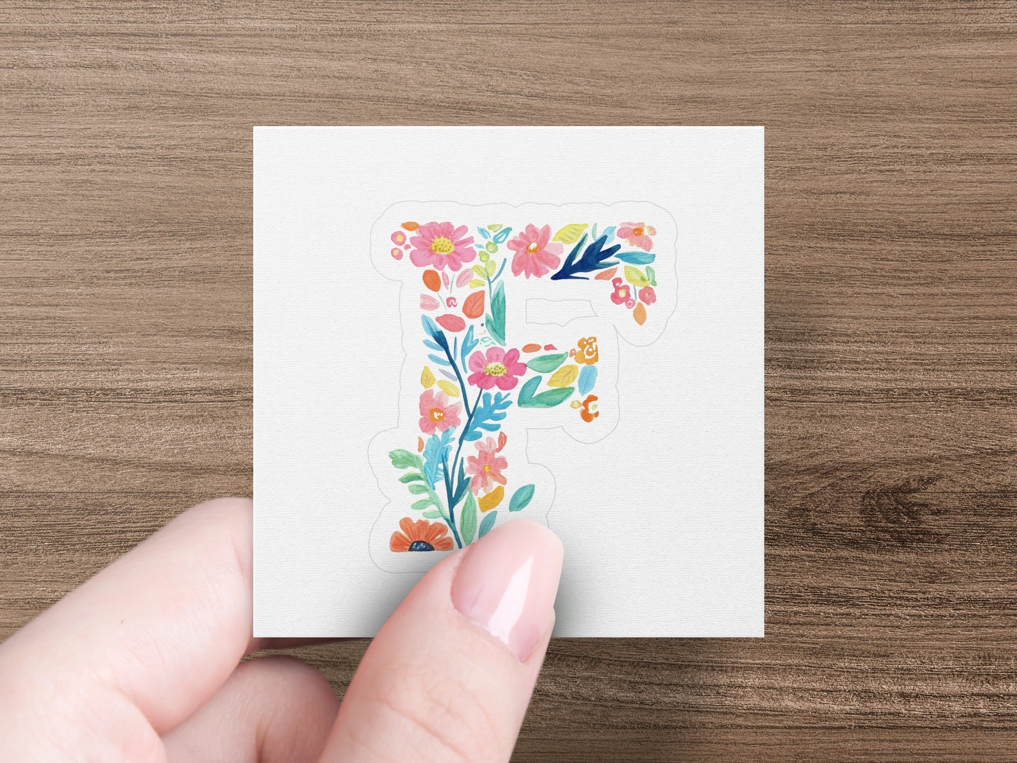 Floral letter F sticker in a hand against a white background.