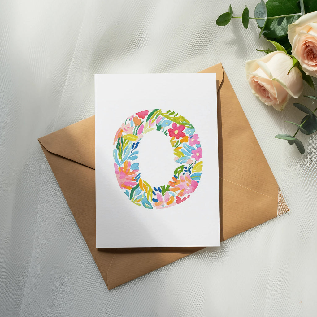 Watercolor floral letter O on a card atop a brown envelope with roses.