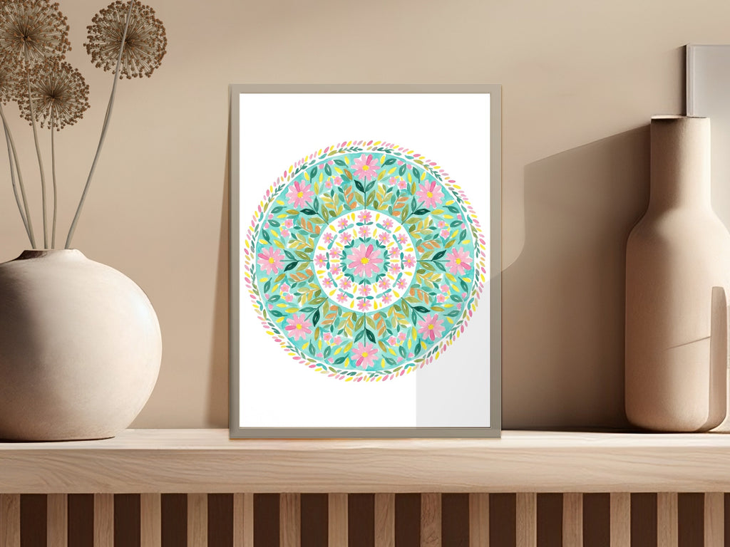 Circular floral mandala art in a white frame on a wooden shelf.