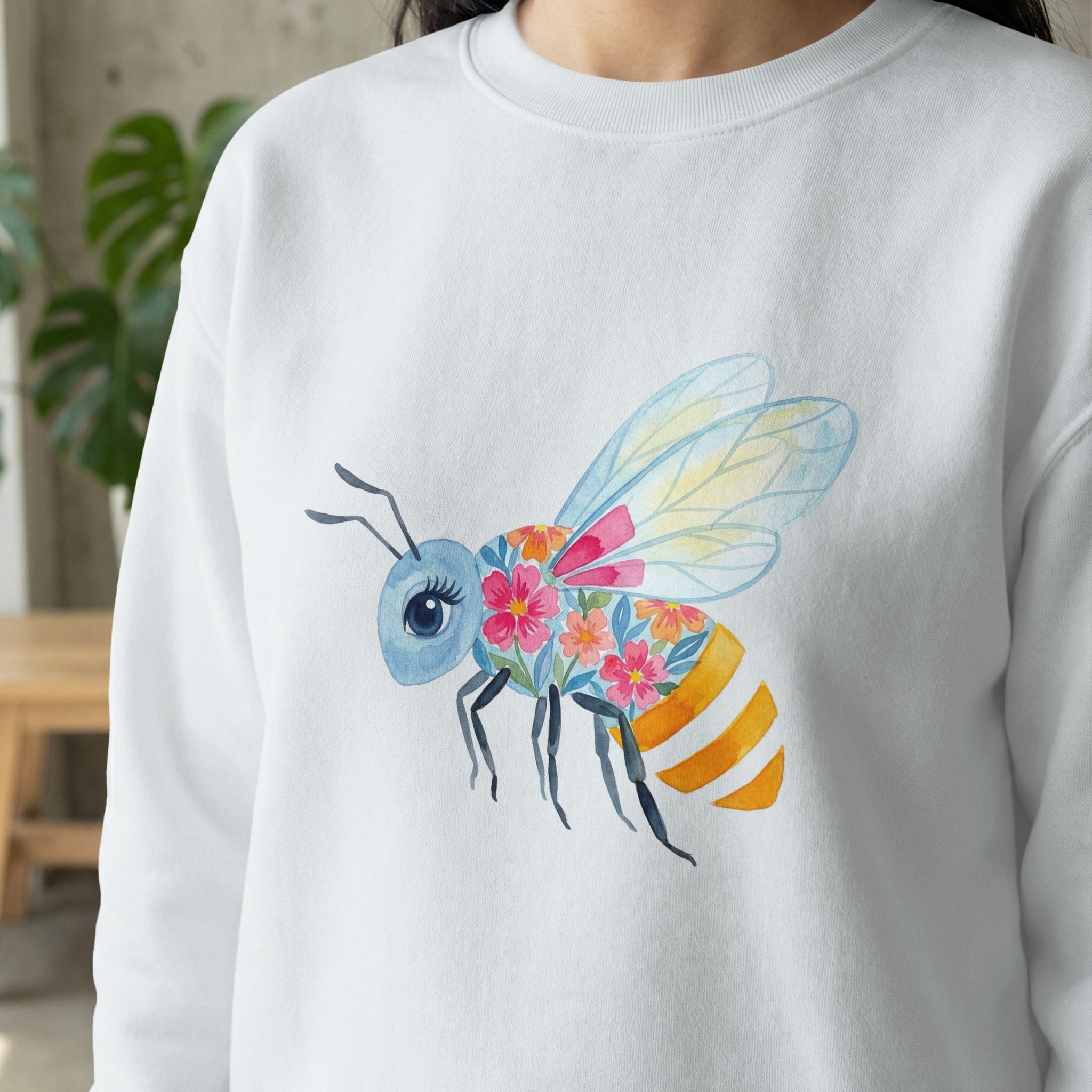 Watercolor bee with floral wings and orange stripes on a white sweatshirt.