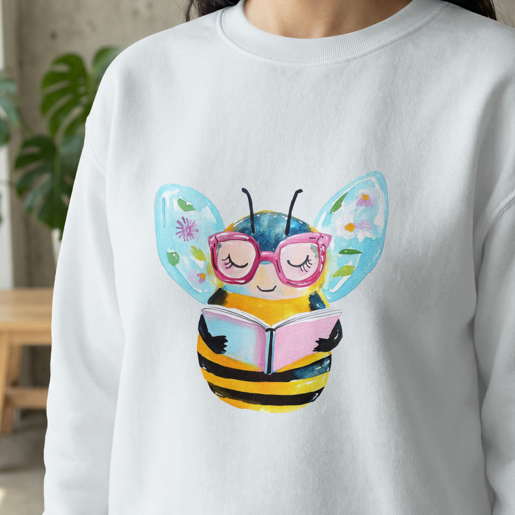 White sweatshirt with watercolor bee wearing glasses reading a book.