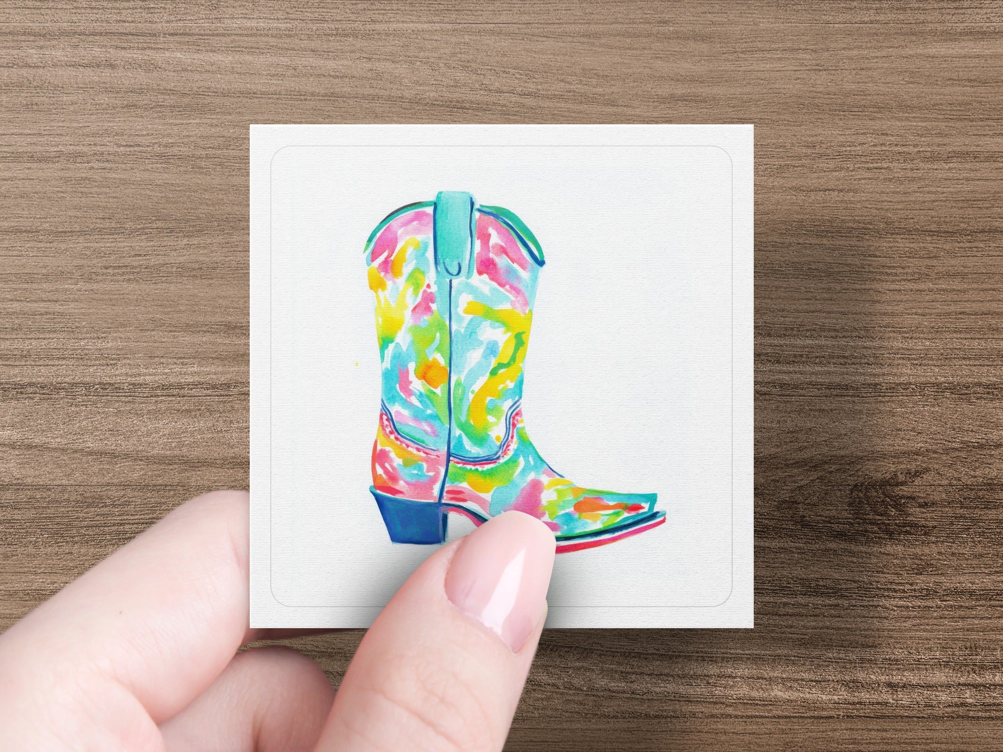 Colorful watercolor cowboy boot on white card held by fingers.