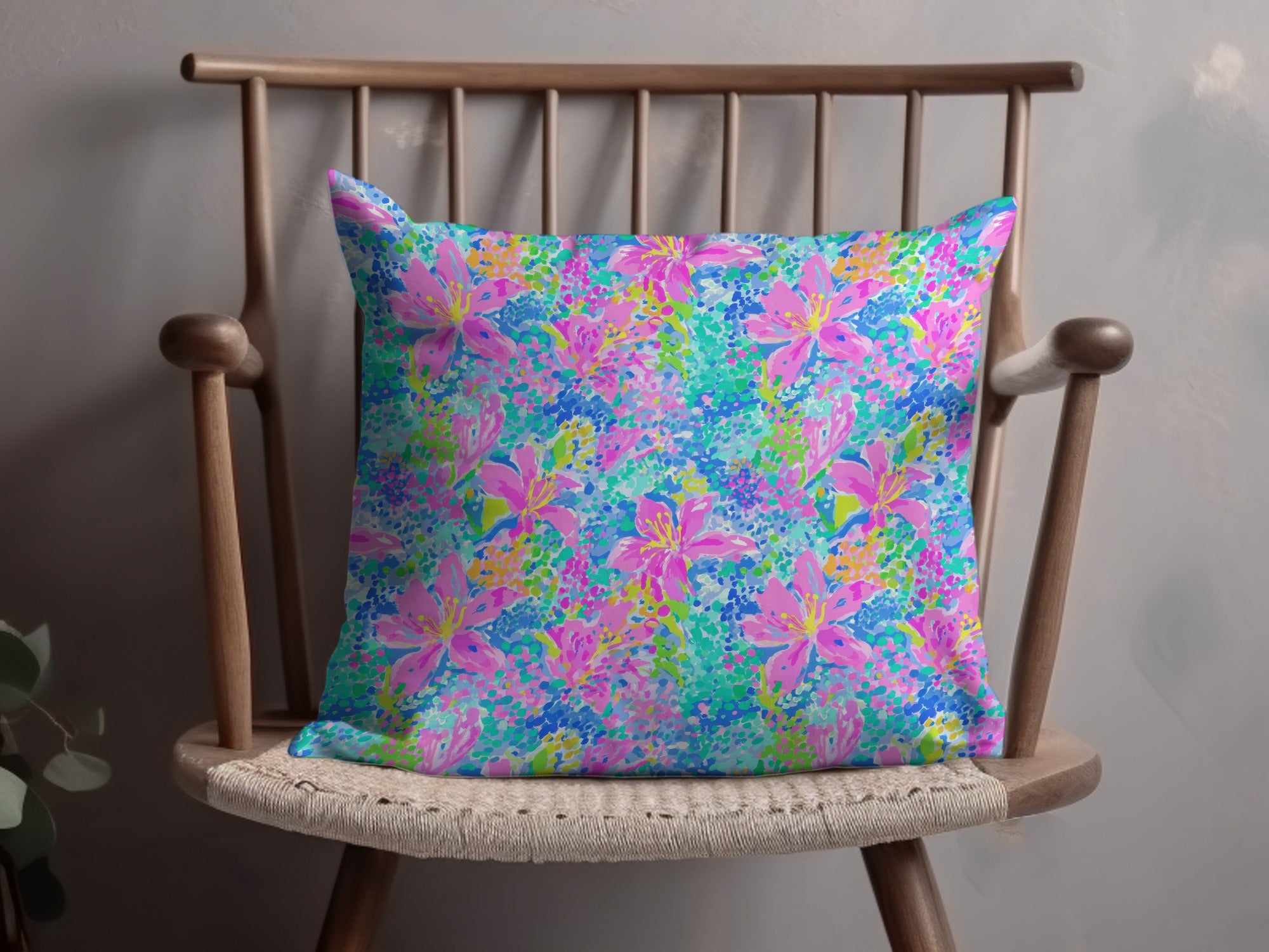 Pink and blue floral print pillow on a wooden chair.