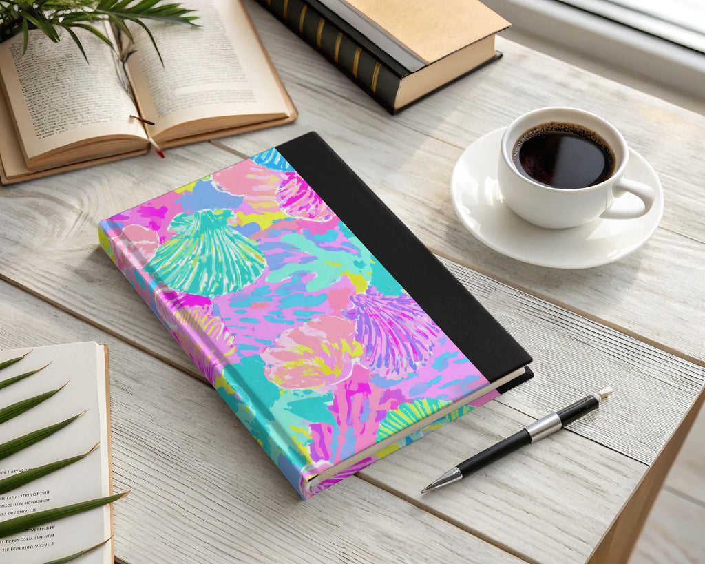 Journal with a colorful seashell pattern, open book, and coffee cup.