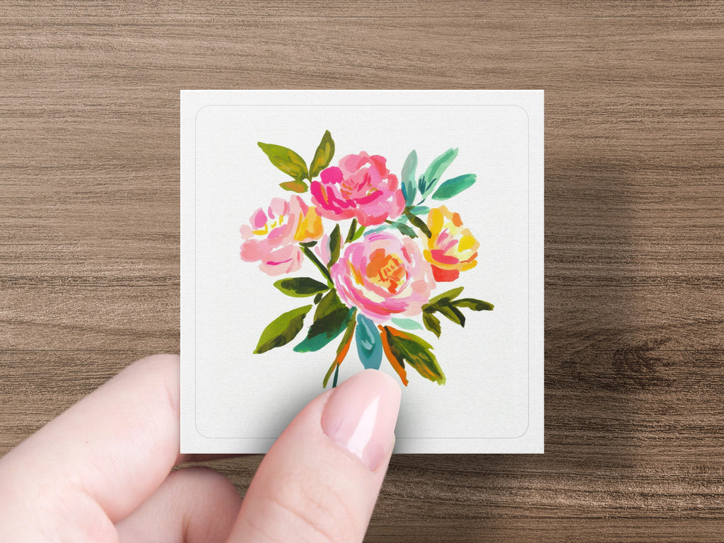 Hand holding a square card with a watercolor painting of pink and yellow roses.