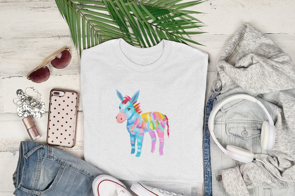 White t-shirt with colorful watercolor donkey graphic, on a flat lay with jeans and headphones.