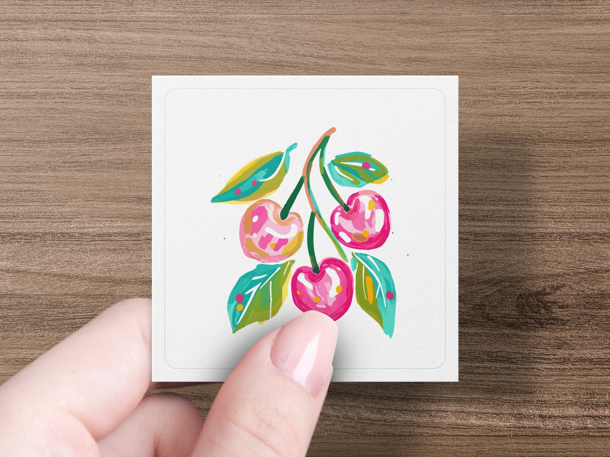 Hand holding card with painted cherries and leaves.