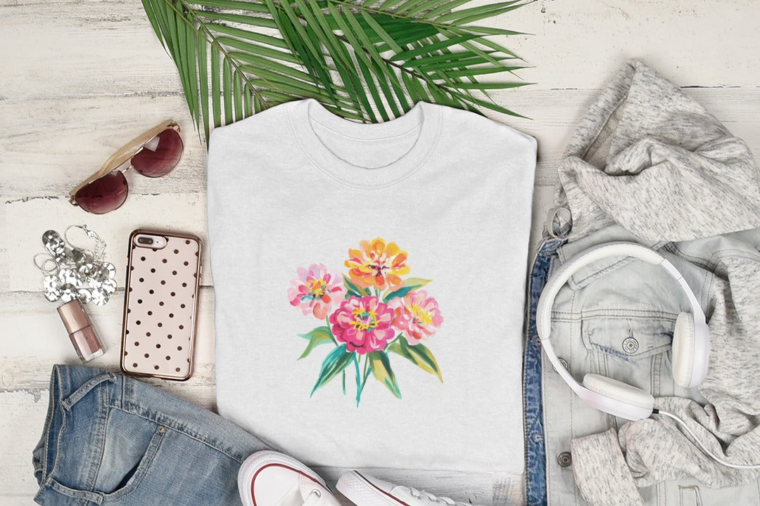 White t-shirt with watercolor floral bouquet design, laid flat with clothing and accessories.