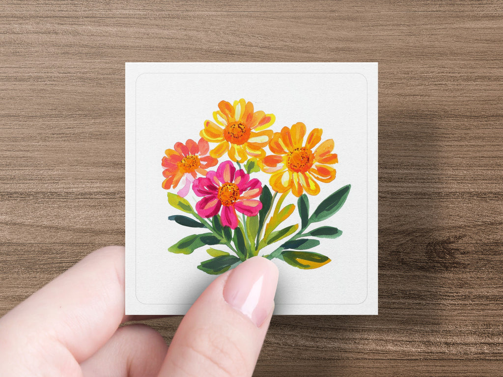 Hand holding a card with a painting of colorful orange and pink flowers.