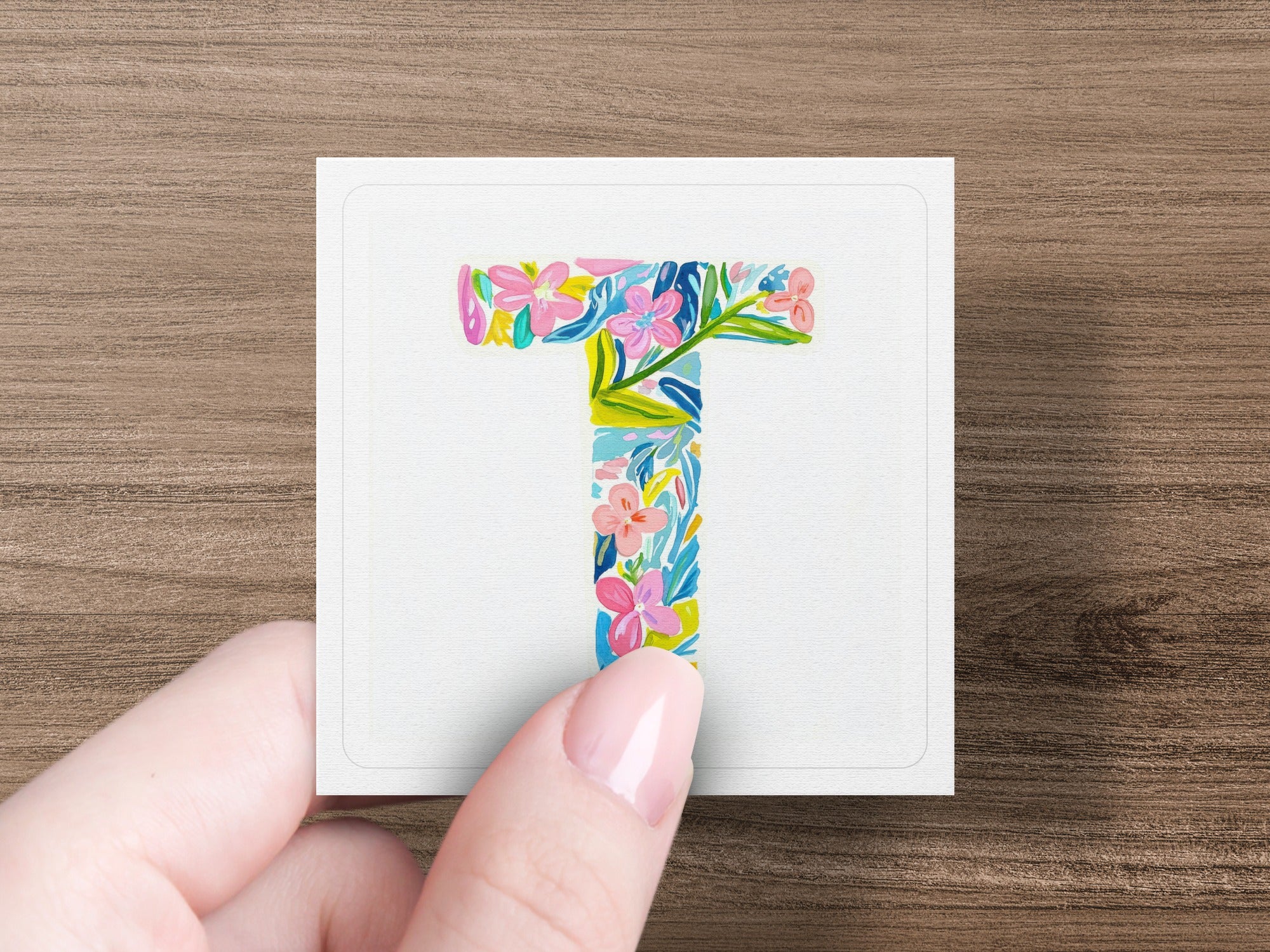 Floral letter T on white card held by hand.