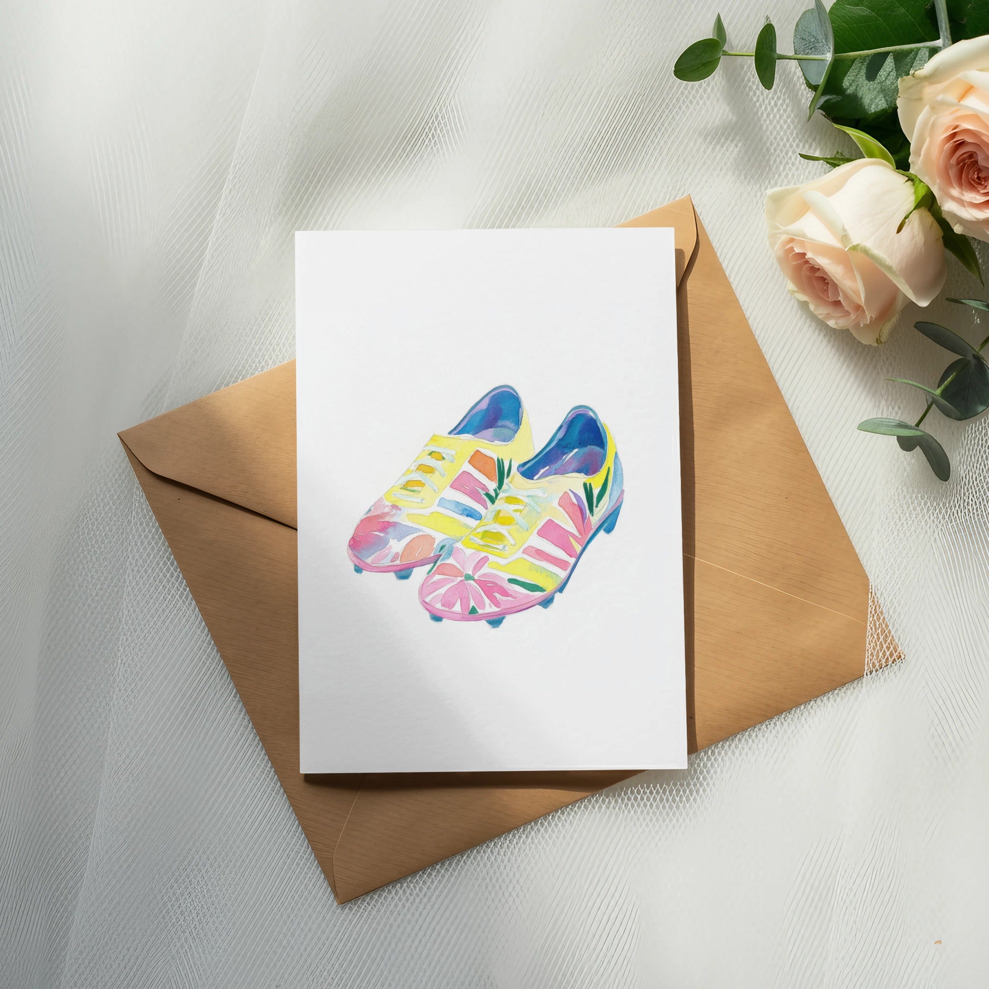 Watercolor painting of colorful soccer cleats on a white card and brown envelope.