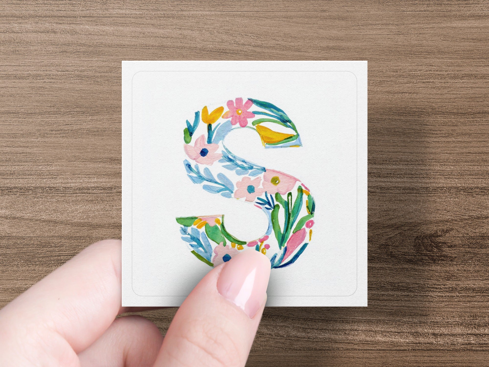Hand holding watercolor letter S with floral pattern.