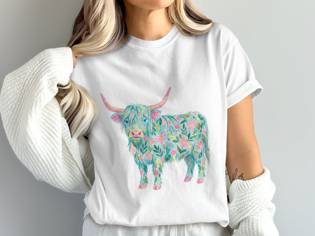 White t-shirt with a watercolor Highland cow design featuring floral patterns.