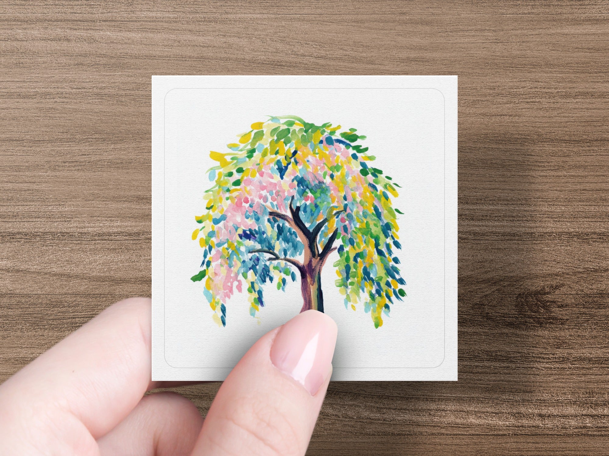 Watercolor painting of a whimsical tree with colorful leaves held by a hand.