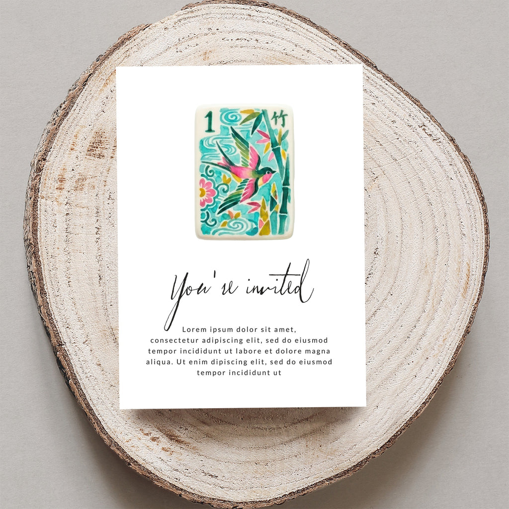 Card with "You're invited" and floral bird design, on wood slice.