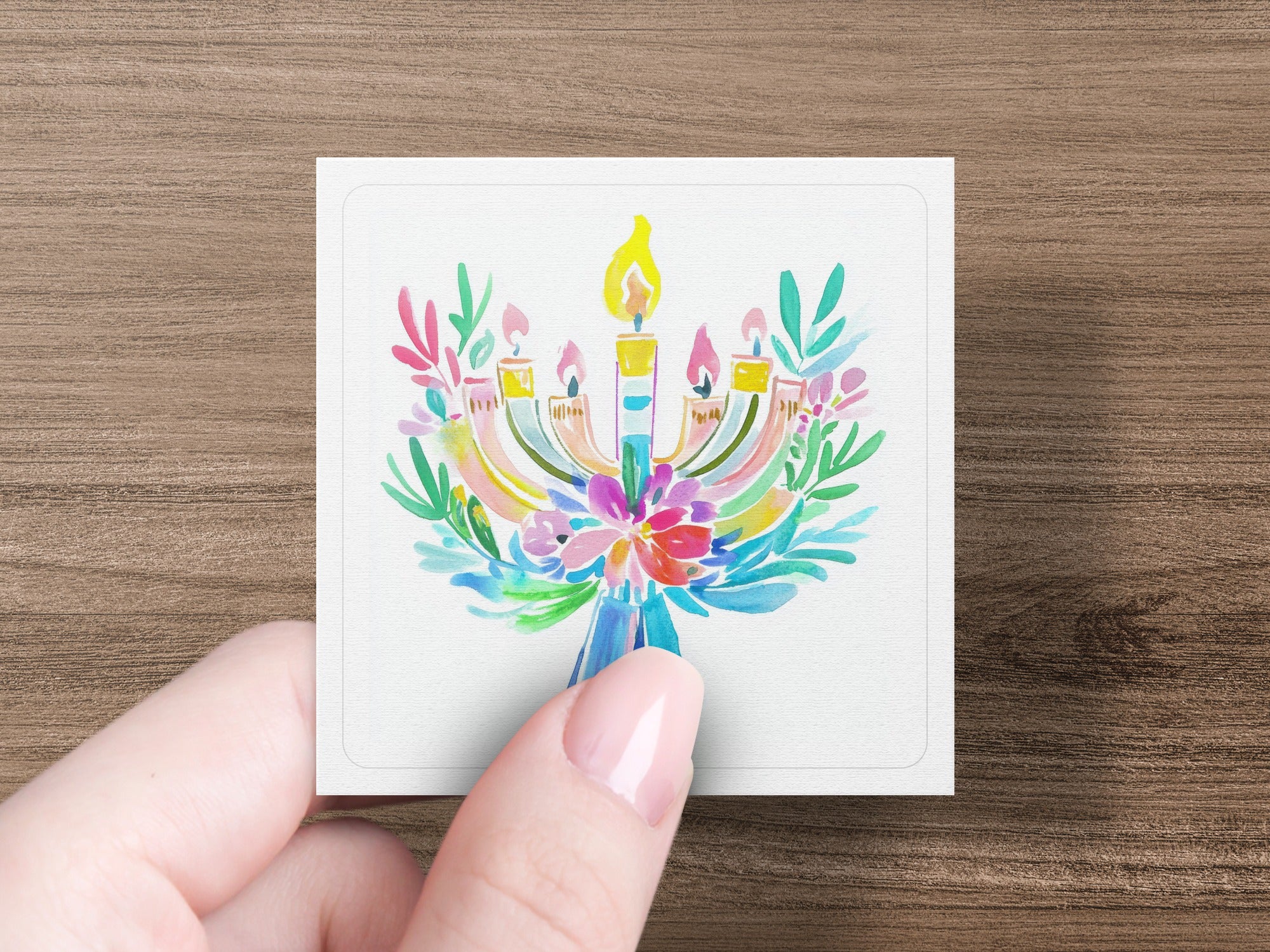 Hand holding a watercolor menorah with colorful floral accents.