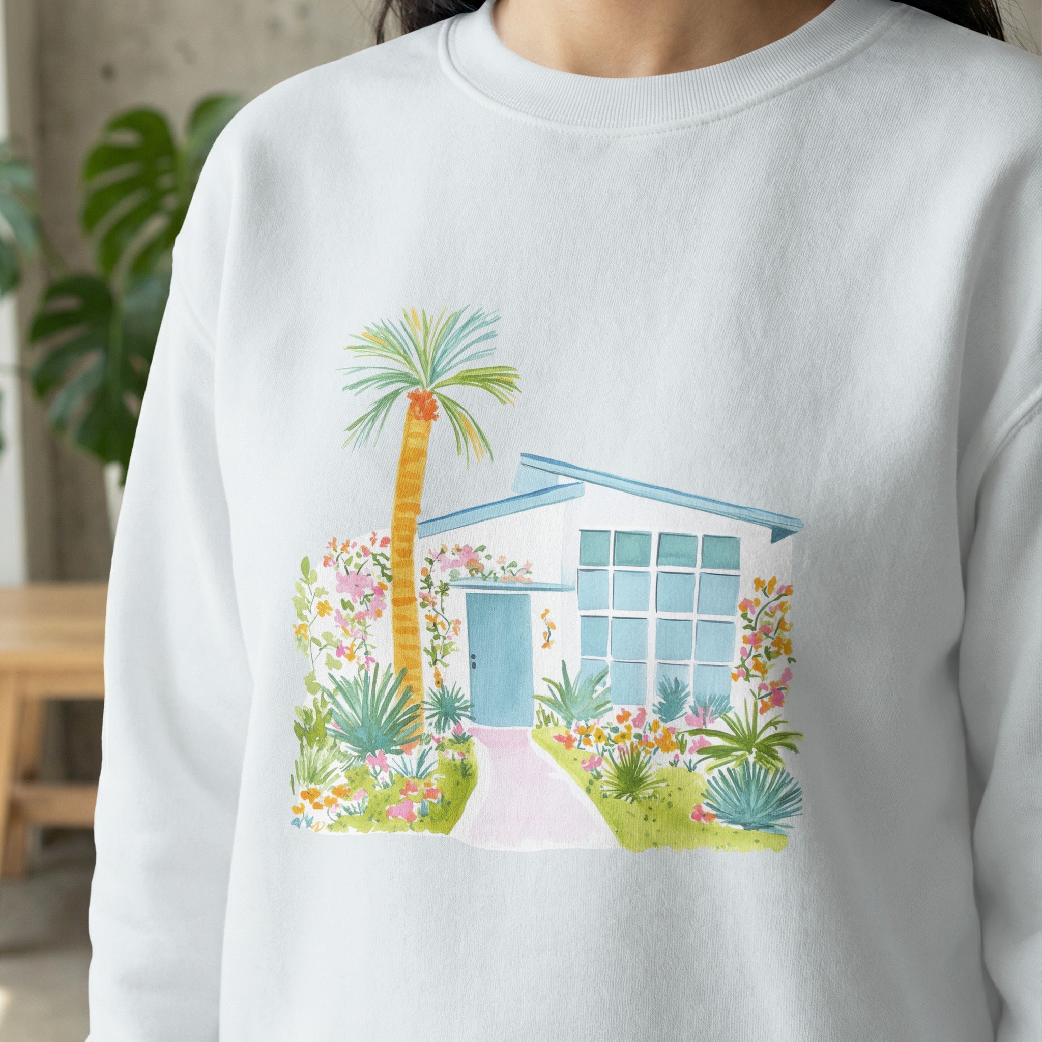 Sweatshirt with watercolor illustration of a modern home and tropical plants.