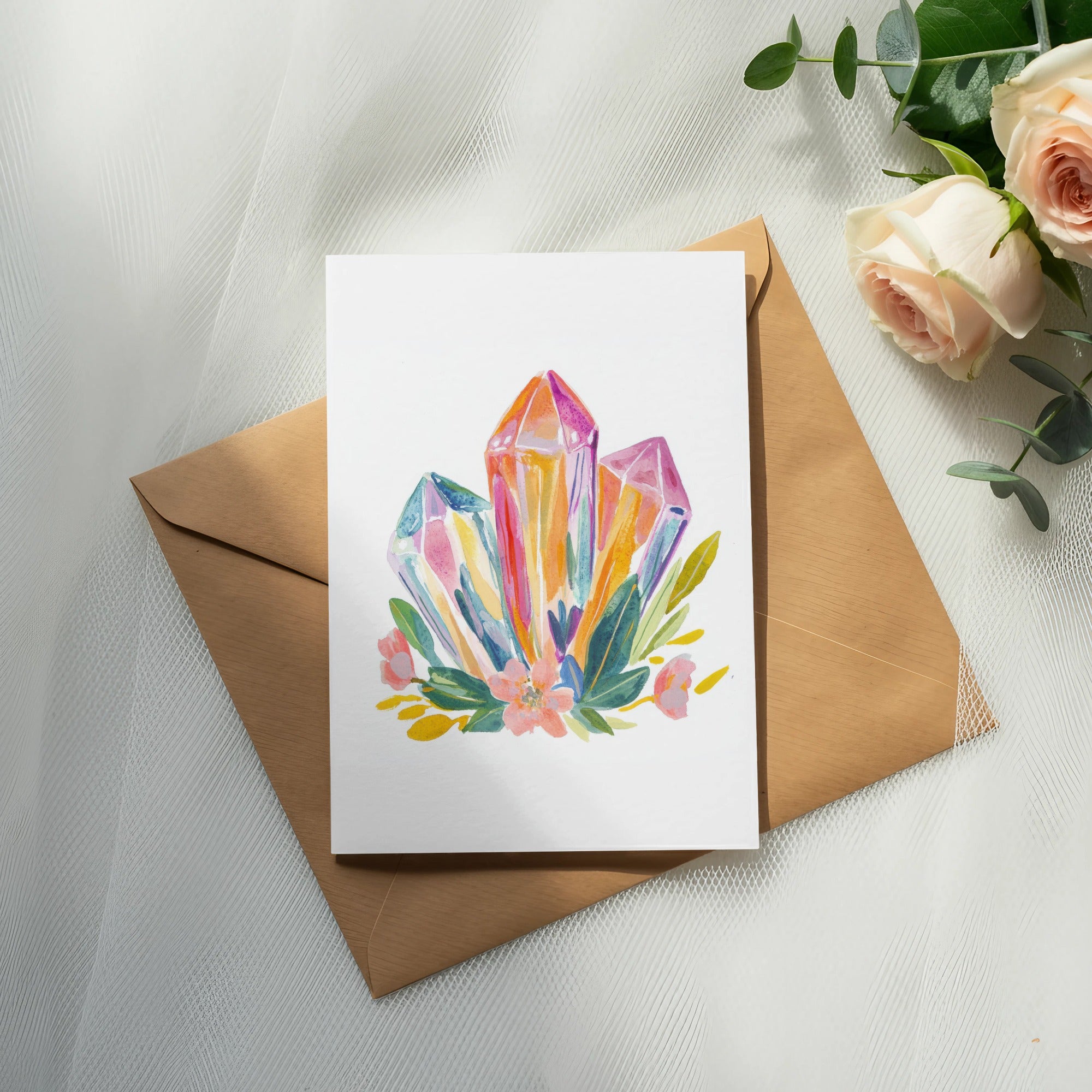 Watercolor illustration of colorful crystals and flowers on a card, resting on an envelope.